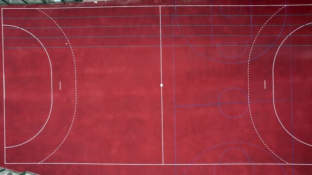 Red multi-purpose sports court seen from above, showcasing distinct white and blue lines marking areas for different activities like soccer, handball, and basketball