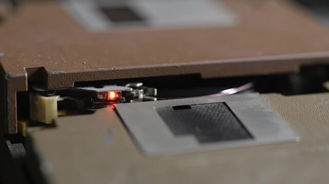 Close-up of a vintage floppy disk drive read-write head with a glowing red indicator light