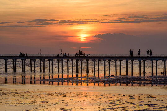 Silhouette of people on a concrete pier over the sea during a dramatic golden sunset.