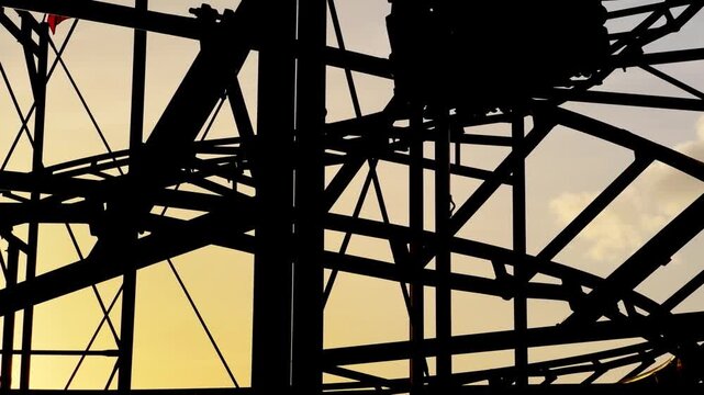 Fast driving cart with people on roller coaster tracks silhouetted against the backdrop of a serene evening sky