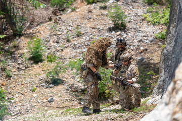 Obraz premium Military special forces team training session outdoor, soldiers in camouflage assisting injured teammate during tactical operation near rock cliff