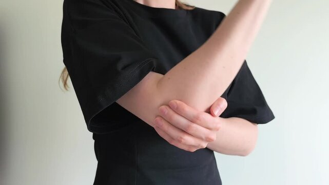 Woman holds her elbow with her hand reacting to sudden pain after an injury. She grips her arm tightly feeling discomfort in the joint. Concept of elbow injury, bruise and joint pain..
