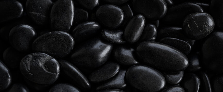 Dark smooth black pebbles background with glossy texture and minimalist zen spa aesthetic