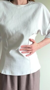 Young woman holding her left side in pain, discomfort in the abdominal area, possible kidney, pancreas or spleen problem, health issue concept, close up view of female torso in casual
