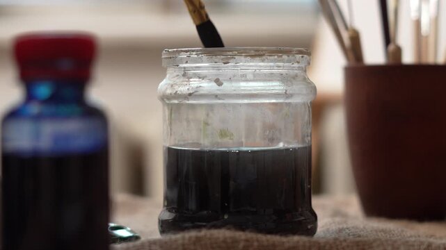 Close-up of an artist washing paint residue from his brush in a jar of water