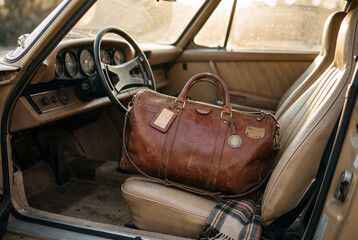 Obraz premium Brown leather duffel bag with football on it on tan seat in classic car