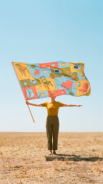 Person waving furniture patterned flag in vast empty golden field