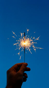 Hand holding a glowing sparkler against deep blue evening sky