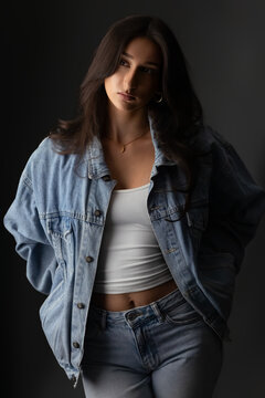 Youth fashion portrait of a confident young woman modern style and beauty. Female model wearing a denim jacket, white top, and jeans, embodying casual wear and contemporary trends. Studio shot with so