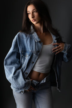 Youth fashion and modern style, confident young woman individuality in a denim jacket and jeans. Female beauty and self expression, model posing with a crop top in a studio setting. Casual wear and ur