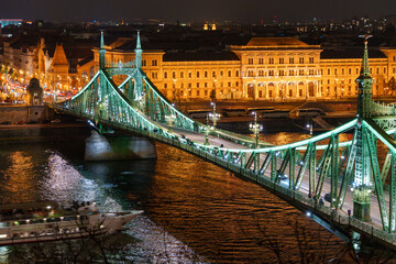 Naklejka premium Illuminated panoramic view of a Liberty bridge crossing the Danube River through historic downtown Budapest Hungary dramatic European architecture night cityscape travel landmark