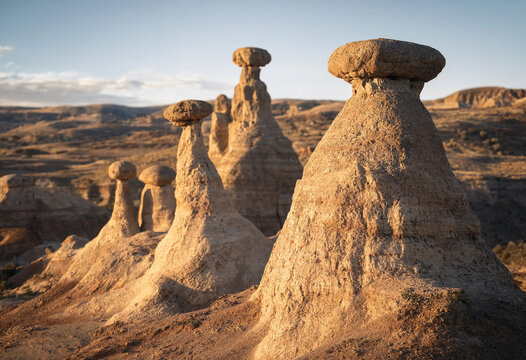 Tall sandstone hoodoo rock formations with capstones standing in a desert landscape under a clear sky during the golden hour sunset light