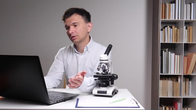 Man experiences confusion and frustration while working remotely from a home office or laboratory setup, analyzing data on a laptop with a microscope on his desk