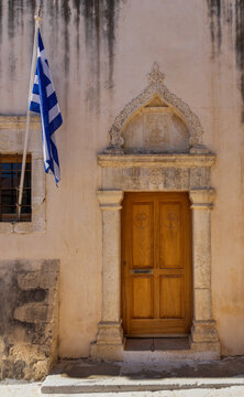Architectural close-up detail of the traditional entrance door of Zoodochos Pigi church featuring the Greek national flag in Gouves, Crete, Greece