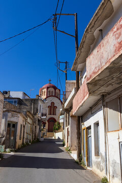 Picturesque narrow street in Gouves village, Crete, Greece, with the historic Zoodochos Pigi church visible in the background under a sunny sky