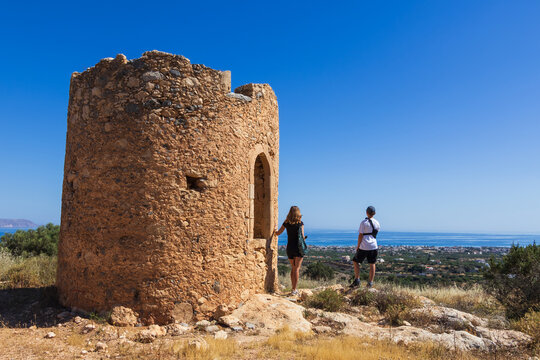 Mother and young son with an arm brace standing at the Gournes Gouvon rotunda viewpoint, looking down at Kato Gouves village and the sea in Crete, Greece