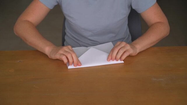 Woman folding a paper airplane from a sheet at a table, high quality audio recording. Soft paper folding sounds and careful hand movements. Creativity, hobby and everyday lifestyle concept.