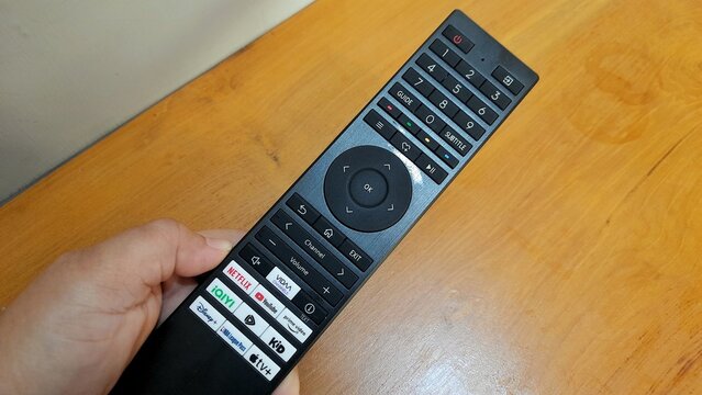 Banyuwangi, East Java, Indonesia - April 29 2026. Hand holding a black smart TV remote control with app buttons