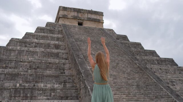 Woman traveler raising hands in front of Kukulkan pyramid in Chichen Itza, Mexico. Slow motion video of female tourist celebrating freedom and travel.