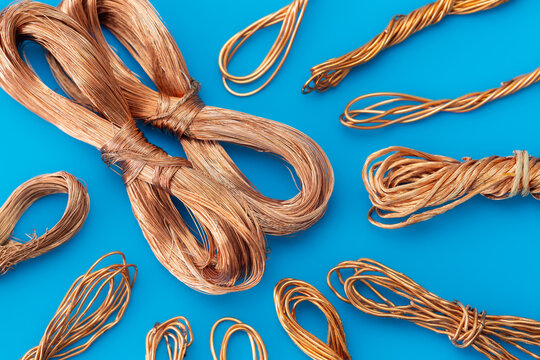 High angle view of pure copper wire bundles on bright blue background. Industrial raw materials for electrical recycling, electronics manufacturing and scrap metal trade.