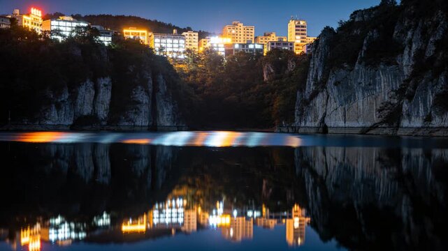 Shifting reflections showing lit hillside buildings framed by cliffs at night, triggered by ripples