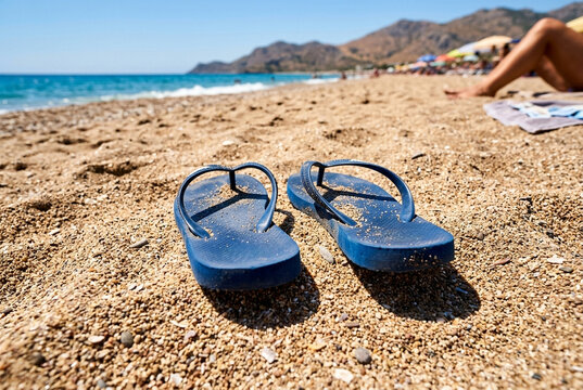 Blue flip flops on sandy beach with ocean waves in background