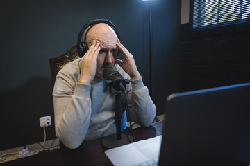 Stressed Man in Podcast Studio Holding Head at Microphone © Dewald