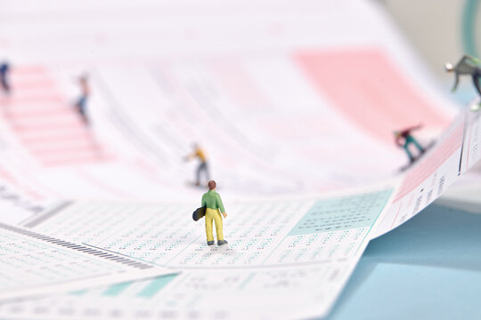 Miniature People on Exam Answer Sheet Representing School Test and Academic Pressure