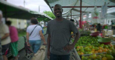 Fototapeta premium African American man standing confidently at open air market surrounded by fresh produce smiling warmly toward camera creating friendly approachable portrait of everyday work