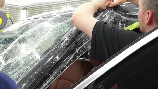 A car wrapping specialist applies a polyurethane film to the car. Detailer smoothes PPF. Car wrapping, detailing, tuning and styling. Selective focus. PPF protective film against chips and scratches. 
