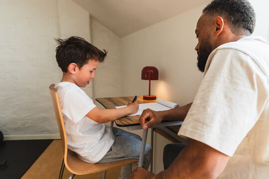 Young boy focusing on writing at desk with father