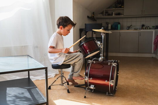 Focused young boy practicing drums in living room