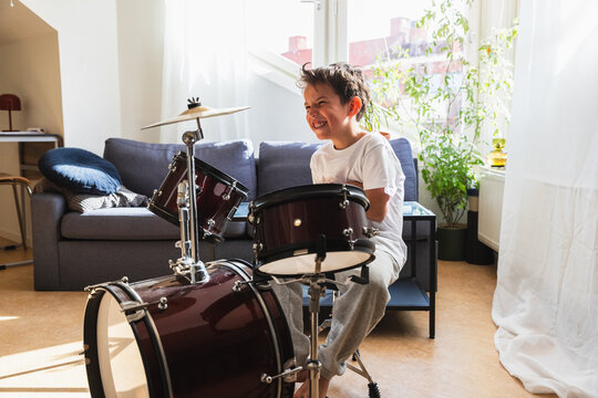 Joyful boy laughing while playing drums at home