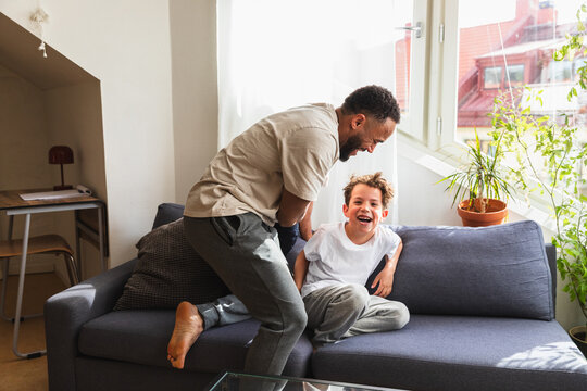 Playful father tickling laughing son on sofa