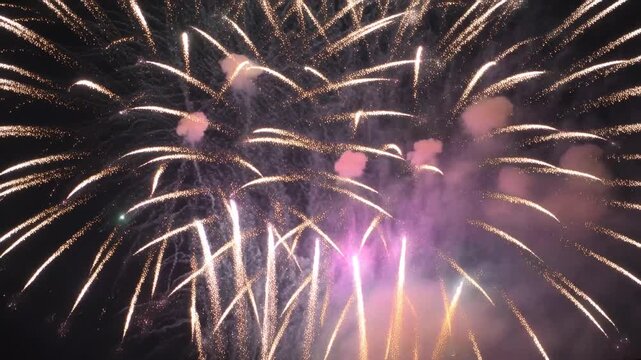 Firing shells, fireworks display forming golden bursts and sparks over night sky, celebrating event