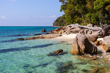Obraz premium Rocky shoreline of Koh Adang in Tarutao National Park, Thailand. Clear turquoise water meets a sandy beach. Tropical greenery and coastal landscape.