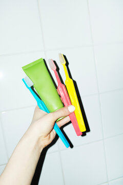 Hand holding toothbrushes and toothpaste in bathroom tile wall