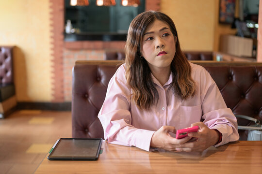 Transgender woman looking up while holding a smartphone in a restaurant