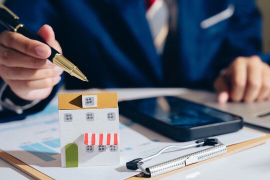 Miniature house model business person pen smartphone clipboard financial document office desk business concept investment planning real estate small building paper chart professional attire