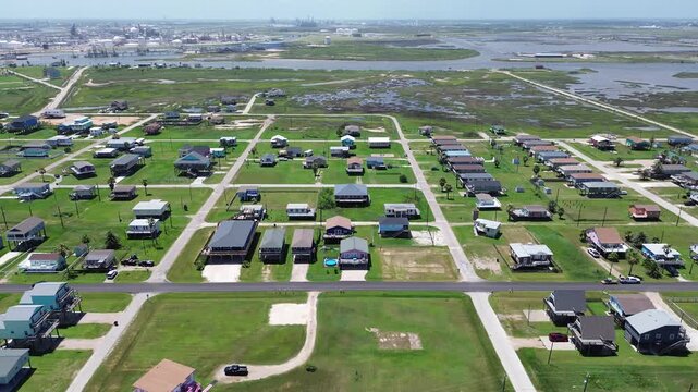 Inlet industrial backdrop residential rows east of Seashell Dr align with paved unpaved roads while tank farms port structures rise across waterway. Mixed roofing hues, green lots, Freeport, TX