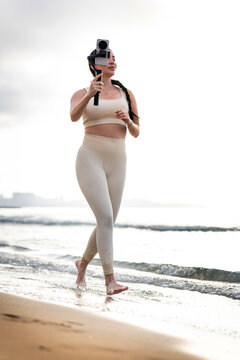 Woman walking on the beach, creating video content for wellness or exercise