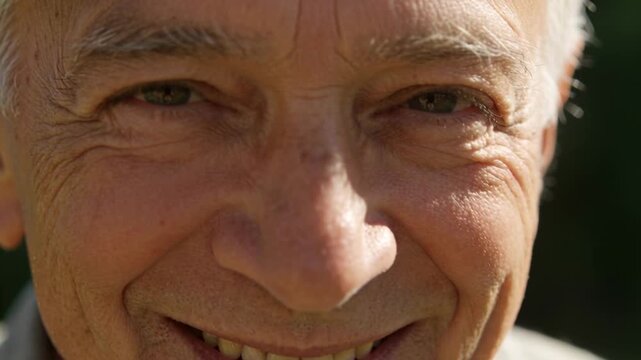 Smiling senior man reacting to sunlight, turning head, squinting in yard, showing teeth and collar