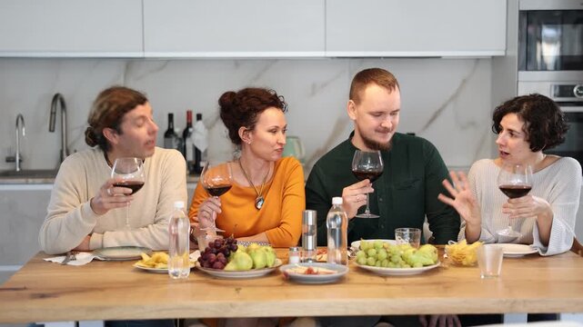 Two married couples are sitting at table, enjoying food and wine, chatting, talking, laughing. In homely atmosphere, friends celebrate anniversary
