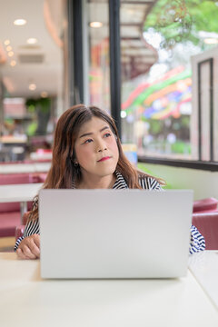 Transgender woman looking up thoughtfully while using a laptop in a cafe