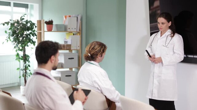 Female doctor gives lecture, uses presentation materials, controls slides using remote control, making presentation. Medical specialists during meeting, medical advisory meeting