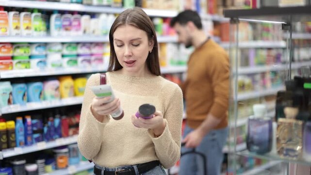 Woman spends time in store, looking for necessary goods and select care product. Attentive customer meticulously studies goods in self-service store, pick up goods