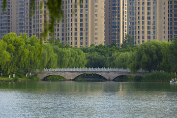 Stone Arch Bridge Across Urban Park Lake with Willow Trees and High Rise Buildings © ThaiKhanh