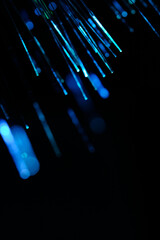 Vertical presentation glowing light blue fiber optic threads radiating against dark background. © freeman83