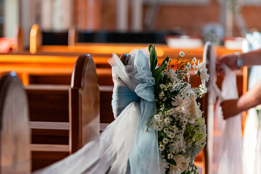 Close up of hands arranging flowers, foliage and tulle on a church pew for wedding ceremony decoration