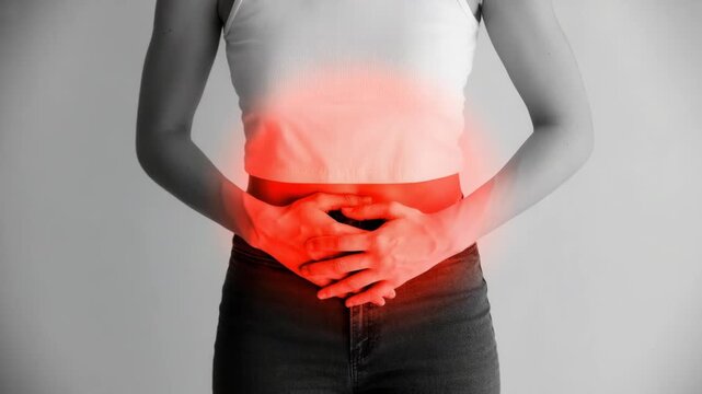 Woman holding her stomach with a red glow on her abdomen indicating pain or discomfort on gray background  health issue